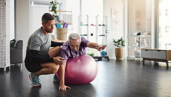 A man on an exercise ball working on causes of arthritis